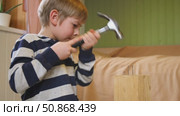 Kid hammers nails to wood with a hammer. Little boy helping with toy tools. Funny 6 years child having fun on building. Kid hammering crafting stuff using wooden pieces. Carpentry and family concept. Стоковое видео, видеограф Марина Демидюк / Фотобанк Лори