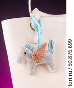Close-up of an elegant bag charm featuring a Pegasus-shaped pendant encrusted entirely with sparkling rhinestones on white  bag. Стоковое фото, фотограф Виталий Сова / Фотобанк Лори