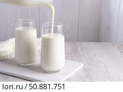 Pouring homemade kefir, buttermilk or yogurt with probiotics. Yogurt flowing from glass bottle on light background. Probiotic cold fermented dairy drink. Trendy food and drink. Copy space. Стоковое фото, фотограф Наталия Попова / Фотобанк Лори