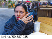 Young woman playfully licking her fingers after a meal at an outdoor food market. Стоковое фото, фотограф Виктор Ветошкин / Фотобанк Лори