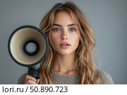 Portrait of a young woman with natural make-up and loose light-brown hair holding a megaphone. The girl is looking straight at the camera with a serious and focused expression. The background is neutral, gray, the focus is on the face and the megaphone. The image symbolizes expression of opinion, voice, activism, communication, leadership and social issues. Стоковое AI-изображение, AI-художник Анна Кривицкая / Фотобанк Лори