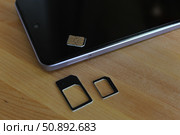 Сим карта лежит на смартфоне и рядом переходники для сим карт других размеров. Стоковое фото, фотограф Ирина Григорьева / Фотобанк Лори