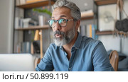 An expressive mature man with salt-and-pepper hair reacts with wide-eyed surprise while engaged with a screen in a contemporary home setting. Стоковое AI-видео, аниматор Данила Большаков / Фотобанк Лори
