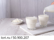 Pouring homemade kefir, buttermilk or yogurt with probiotics. Yogurt flowing from glass bottle on light background. Probiotic cold fermented dairy drink. Trendy food and drink. Copy space. Стоковое фото, фотограф Наталия Попова / Фотобанк Лори