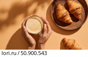Coffee croissant breakfast food pastry morning warm caffeine bakery cozy brown with soft buttery flavor. Hands cradle the morning drink. A calm scene for lifestyle and culinary themes. Стоковое AI-изображение, AI-художник Александра Троицкая / Фотобанк Лори