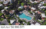 Aerial view revealing luxury resort swimming pool, volcanic rock landscape, verdant gardens, sunbathing areas, and neighboring residential structures. Стоковое AI-видео, аниматор Данил Руденко / Фотобанк Лори