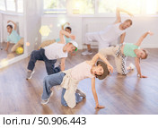 Young girl and group of children in casual wear training hip hop movements on floor in dance class with male coach. Стоковое фото, фотограф Яков Филимонов / Фотобанк Лори