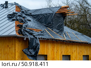Construction of a building with a partially finished roof covered with black plastic sheeting and exposed wooden beams, showcasing the work in progress. Стоковое фото, фотограф Данила Большаков / Фотобанк Лори