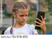 A little girl focused on a phone screen with an expression of puzzlement or concentration. Стоковое фото, фотограф Данила Большаков / Фотобанк Лори
