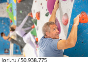 Concentrated elderly man moving on bouldering wall in climbing gym. Стоковое фото, фотограф Яков Филимонов / Фотобанк Лори