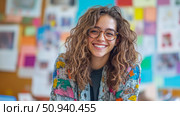 A young woman's close-up portrait with curly hair and eyeglasses, smiling warmly against a colorful classroom-like setting. Стоковое AI-изображение, AI-художник Данила Большаков / Фотобанк Лори