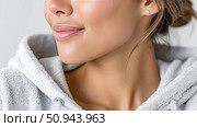 Woman in grey hoodie smiling softly against a neutral background. Стоковое AI-изображение, AI-художник Katsiaryna Repich / Фотобанк Лори