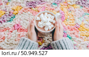 Winter Holiday: A cozy cup of hot chocolate with marshmallows held by hands over a pastel chunky knit blanket. Стоковое AI-изображение, AI-художник Данила Большаков / Фотобанк Лори