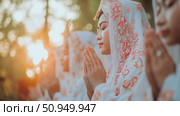 Spiritual Moment: A group of young women in traditional dress are praying, heads bowed, during a religious ceremony. Стоковое AI-изображение, AI-художник Данила Большаков / Фотобанк Лори