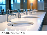 A modern restroom showcases seamless integration of under-mount sinks in white quartz countertops. Automatic fixtures and diffused lighting create an inviting and high-tech environment. Стоковое AI-изображение, AI-художник Nart / Фотобанк Лори