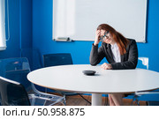 Tired red-haired business woman in glasses and a suit alone in an empty conference room. An office worker with a headache is waiting for the presentation to begin in the boardroom. Стоковое фото, фотограф Михаил Решетников / Фотобанк Лори