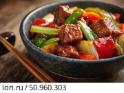 Sweet sour pork with colorful peppers, mixed vegetables served in a black bowl on dark concrete background. Traditional Chinese dish. Close-up. The meat pieces in a brown sauce glaze. Sichuan cuisine. Стоковое AI-изображение, AI-художник Марина Демидюк / Фотобанк Лори