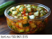 Fresh salad of cucumbers, tomatoes and greens in a transparent glass bowl. The pieces of vegetables are cut into cubes, seasoned with aromatic spices, garlic, sesame and greens. The dish looks bright, juicy and appetizing, ideal for healthy eating, vegetarian menu and summer lunch. The background of warm wood adds home comfort and emphasizes the naturalness of the composition. Стоковое AI-изображение, AI-художник Анна Кривицкая / Фотобанк Лори