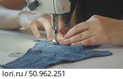 A close-up shot of a seamstress's hands working with sewing machines on a piece of denim fabric, which is pierced with pins. Стоковое видео, видеограф Strunov David / Фотобанк Лори