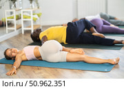 Young woman coach and students perform Supta Ardha Matsyendrasana during training in studio. Стоковое фото, фотограф Яков Филимонов / Фотобанк Лори