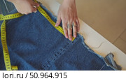 Hands are adjusting measuring tape on the denim material, marking it with a piece of chalk. Стоковое видео, видеограф Strunov David / Фотобанк Лори