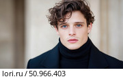 Compelling gaze of a young man with striking blue eyes and wavy brown hair, clad in a sleek black turtleneck, conveying calm confidence for editorial media. Стоковое AI-изображение, AI-художник Данила Большаков / Фотобанк Лори