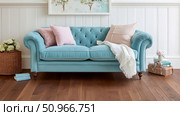A charming and cozy home interior with a teal velvet tufted sofa adorned with soft pillows and a white throw blanket, set against a paneled wall and rich wooden floor. Стоковое AI-изображение, AI-художник Данила Большаков / Фотобанк Лори