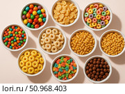 Colorful assortment of cereals and candies in white bowls. Various shapes and sizes, including rings, loops, and chocolate balls. Bright and vibrant colors. Стоковое AI-изображение, AI-художник Nart / Фотобанк Лори