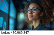 A visionary professional woman with curly hair and stylish glasses intently studying intricate data on large, illuminated screens, embodying innovation, analysis, and future-forward thinking in a high-tech environment. Стоковое AI-изображение, AI-художник Данила Большаков / Фотобанк Лори