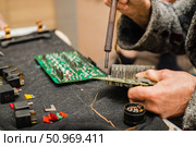 Person is soldering a circuit board, surrounded by electronic components, fuses, and other tools. Стоковое фото, фотограф Алёна Золотухина / Фотобанк Лори