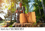 Man chopping firewood with axe in forest on sunny summer day, close-up of splitting log and flying wood chips, outdoor rural work in nature with lumberjack wearing overalls. Harvesting of firewood. Стоковое фото, фотограф Сергей Тимофеев / Фотобанк Лори