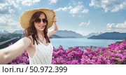 European woman travel blogger in a straw hat and sunglasses takes a selfie photo at the observation point Rachaphrapha dam Cheo Lan Lake in Khao Sok Park in Thailand. Solo travel in Southeast Asia. Стоковое фото, фотограф Владимир Разгуляев / Фотобанк Лори