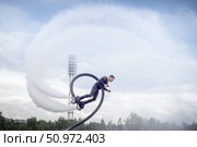 An athlete showcases their flyboarding skills, soaring above the water with jets of water propelling them into the air. The setting features clear skies and a lush background, Стоковое фото, фотограф Владимир Разгуляев / Фотобанк Лори