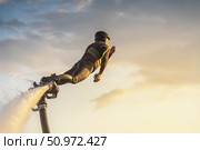 A flyboarder displays skill and excitement while soaring above the water during a stunning sunset. The bright colors of the sky create a dramatic backdrop as the rider navigates through the air. Стоковое фото, фотограф Владимир Разгуляев / Фотобанк Лори