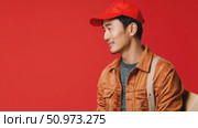 Smiling Asian man in a vibrant red cap and brown jacket portraying a cheerful messenger ready for service. Стоковое AI-видео, аниматор Данила Большаков / Фотобанк Лори