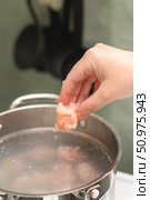 Woman's hand dropping frozen chicken meatball into boiling pot for homemade soup preparation, cooking process close-up with steam. Стоковое фото, фотограф Татьяна Степанищева / Фотобанк Лори