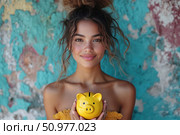 A young woman with a warm smile holds a bright yellow piggy bank in her hands. In the background is a vintage multi-colored wall with cracked plaster in turquoise and pink shades, creating an atmosphere of coziness and creativity. The girl is wearing a summer top, her image is light, sunny and inviting. The concept of the photo is financial literacy, savings, youth, a positive attitude towards money and confidence in the future. Ideal for topics related to personal finance, savings, saving, banks, investments and motivation. Стоковое AI-изображение, AI-художник Анна Кривицкая / Фотобанк Лори