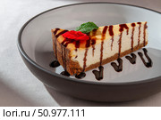 Baked cheesecake with graham crust and chocolate sauce, garnished with mint leaf and flower on a ceramic plate in soft daylight. Стоковое фото, фотограф Aleksandr Gavrilychev / Фотобанк Лори