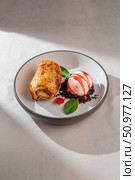 An appetizing golden-brown apple strudel beautifully paired with a scoop of creamy vanilla ice cream drizzled with berry sauce and fresh mint leaves. Стоковое фото, фотограф Aleksandr Gavrilychev / Фотобанк Лори