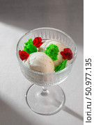 Three creamy scoops of vanilla ice cream beautifully presented in a classic glass dessert bowl, adorned with vibrant red roses and green decorative elements. Стоковое фото, фотограф Aleksandr Gavrilychev / Фотобанк Лори