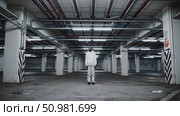 Lone male standing centrally within shadowy parking garage, white tracksuit contrasting against gritty concrete walls featuring urban graffiti markings. Стоковое AI-видео, аниматор Данил Руденко / Фотобанк Лори