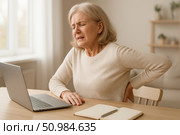 Elderly woman experiences back pain while using laptop at home, highlighting health risks of poor posture and sedentary work. Senior woman with back pain working at laptop. Стоковое AI-изображение, AI-художник Башкирова Анна / Фотобанк Лори
