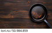 Cooking surface showing residue in a cast iron skillet on wooden table. Стоковое AI-изображение, AI-художник Katsiaryna Repich / Фотобанк Лори