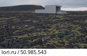 Minimalist concrete structure emerging from barren volcanic terrain, stark lava field surrounding angular building, muted colors merging with dramatic overcast Icelandic skyline. Стоковое AI-видео, аниматор Данил Руденко / Фотобанк Лори