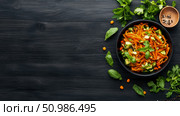 Vibrant top-down view of healthy plant-based noodle dish with fresh vegetables and aromatic herbs, artfully arranged on dark rustic wooden surface with scattered spices. Стоковое AI-изображение, AI-художник Данила Большаков / Фотобанк Лори