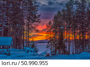 Winter evening in the forest with a view of the lake, painted by a bright sunset. Between the snow-covered pines you can see the road leading to the frozen water, along which the car is moving. The sky is ablaze with rich shades of red, orange, purple and yellow, creating a contrast with the cold blue of the snow. The atmosphere of solitude, northern silence and the beauty of the passing day. Стоковое фото, фотограф Анна Кривицкая / Фотобанк Лори