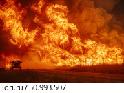 Firestorm engulfing the landscape with a vehicle fleeing the scene, showing the ferocity of natural disasters. Concept: Aftermath of natural disasters. For educational and news materials. Стоковое AI-изображение, AI-художник Лариса Пономарева / Фотобанк Лори