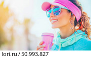 Smiling Woman in Pink Visor and Sunglasses Holding Pink Cup Outdoors. Стоковое AI-изображение, AI-художник Данила Большаков / Фотобанк Лори