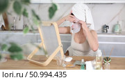 Adult woman in towel turban on head applying hydrating face mask during daily self-care routine after shower at home. Стоковое видео, видеограф Яков Филимонов / Фотобанк Лори