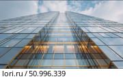 Modern architecture showcases sleek glass facade of high-rise building under blue sky and clouds with natural light at the base. Стоковое AI-видео, аниматор Сергей Толмачёв / Фотобанк Лори